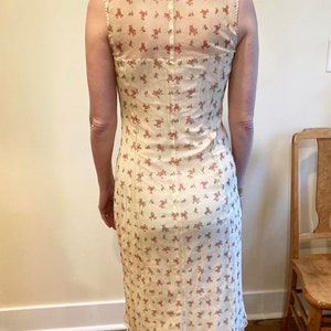 May include: A white midi dress with a floral print and a sheer lace overlay on the back. The dress has a fitted bodice and a flowy skirt.