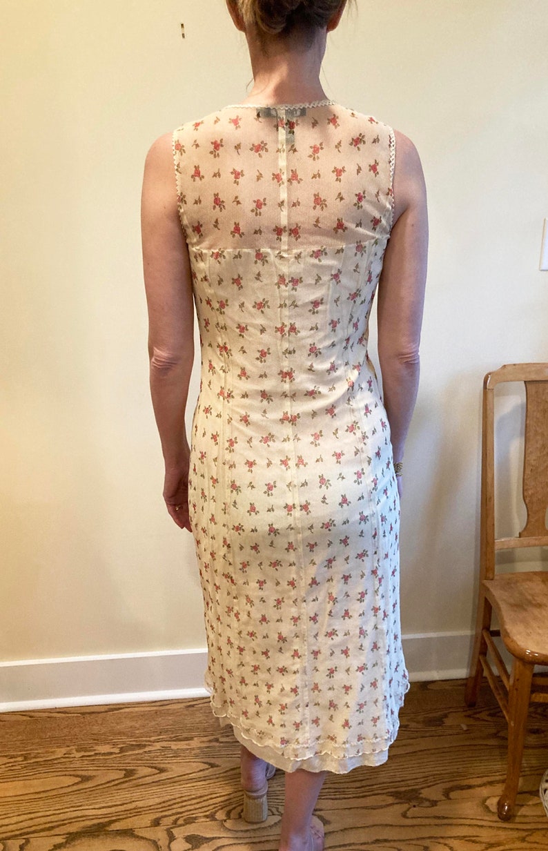 May include: A white midi dress with a floral print and a sheer lace overlay on the back. The dress has a fitted bodice and a flowy skirt.