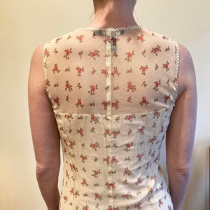 May include: A sleeveless white dress with a floral pattern and a sheer overlay. The dress has a fitted bodice and a flowing skirt.