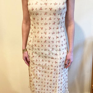 May include: A white sleeveless midi dress with a floral print of small pink roses. The dress has a sheer overlay at the neckline and a lace trim at the hem.