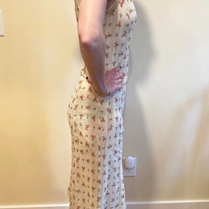May include: A white midi dress with a floral print. The dress has a sleeveless design and a scalloped hem.