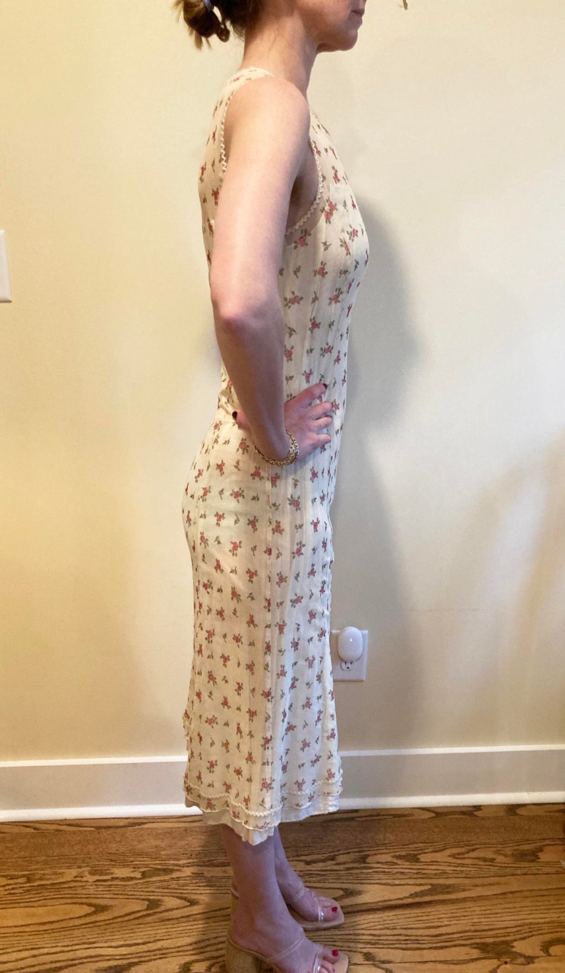 May include: A white midi dress with a floral print. The dress has a sleeveless design and a scalloped hem.