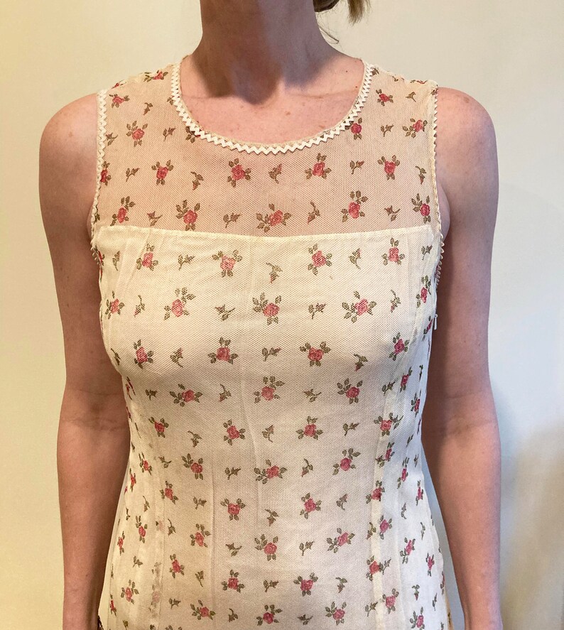 May include: A sleeveless white top with a floral pattern and a lace trim around the neckline.