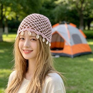 Peut inclure: Un bonnet en crochet rose clair doté d'un motif en maille ajourée et d'un bord festonné orné de petits coquillages cauris blancs suspendus au bas du bonnet, créant un accessoire texturé et décoratif pour la tête.