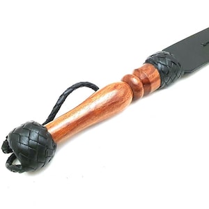 Artisan handmade black leather paddle crafted from genuine leather with a natural wood handle and braided leather accents. Premium leather craftsmanship item, handmade leather accessory, custom leatherwork gift, traditional artisan leather product, rustic handmade decor, leather collector item, quality leather craft, handcrafted leather design, durable leather accessory, unique artisan creation.