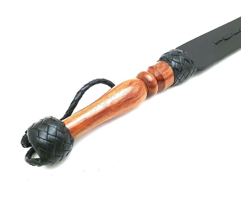 Artisan handmade black leather paddle crafted from genuine leather with a natural wood handle and braided leather accents. Premium leather craftsmanship item, handmade leather accessory, custom leatherwork gift, traditional artisan leather product, rustic handmade decor, leather collector item, quality leather craft, handcrafted leather design, durable leather accessory, unique artisan creation.
