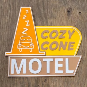 May include: A decorative sign featuring an orange traffic cone with a sleeping car graphic and the letter Z repeated four times. To the right, a yellow panel displays the brown text COZY CONE, and below, a tan rectangular panel features the white text MOTEL.