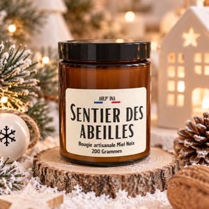 Op de afbeelding: Een bruine glazen kaarsenpot met een zwart deksel en een wit etiket met de tekst AULP' INA, SENTIER DES ABEILLES, Bougie artisanale Miel Noix en 200 Grammes. Het etiket bevat een kleine blauwe, witte en rode horizontale streepafbeelding.