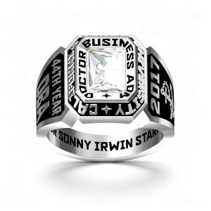 May include: A silver-toned ring featuring a central square clear stone. The bezel is engraved with DOCTOR BUSINESS ADM CALIFORNIA. The sides display 44TH YEAR DBA and 2017 with an anchor emblem. The inner band is engraved with SONNY IRWIN STAR.
