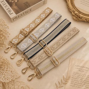 Pode incluir: Cinco alças ajustáveis para bolsa com ferragens metálicas em tom dourado e fechos de mosquetão. As alças apresentam vários padrões tecidos em tons de dourado, bege, branco e azul-marinho, com desenhos geométricos de diamantes e linhas.