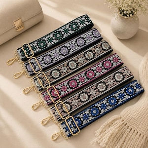May include: Six adjustable bag straps featuring woven floral patterns in green, purple, light blue, pink, white, and dark blue on black backgrounds. Each strap includes gold-toned metal swivel lobster clasps and rectangular sliders for length adjustment.