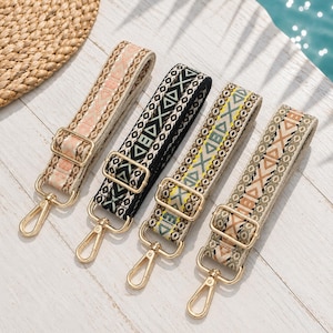 May include: Four adjustable bag straps featuring woven geometric patterns in shades of peach, black, yellow, and tan. Each strap includes gold-toned metal hardware, including a sliding buckle for length adjustment and a swivel lobster clasp at the end.