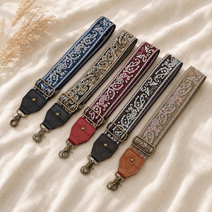 Può includere: Cinque tracolle regolabili con intricati motivi paisley in blu, oro, bordeaux, nero e beige. Ogni tracolla include ganci girevoli e finiture in metallo, con linguette terminali in similpelle di colore nero, rosso o marrone chiaro.