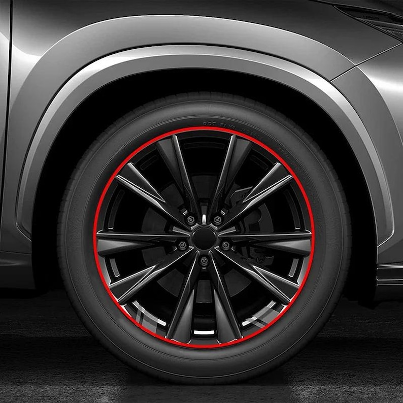 Puede incluir: Una rueda de coche negra con un dise&ntilde;o de radios m&uacute;ltiples y una fina franja decorativa o protector de llanta circular de color rojo vibrante aplicado a lo largo del borde exterior de la rueda, sobre una carrocer&iacute;a gris y un neum&aacute;tico negro.