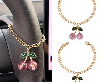 May include: A gold-toned chain bracelet featuring a cherry charm with green enamel leaves and two translucent pink or red spherical beads. The bracelet includes a lobster claw clasp and is shown in two variations with different bead colors.