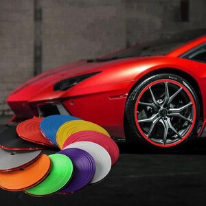 Puede incluir: Una colecci&oacute;n de tiras adhesivas circulares para protecci&oacute;n de llantas en varios colores, incluyendo rojo, azul, amarillo, blanco, morado, verde, naranja, gris y negro, frente a un coche deportivo rojo con un protector de llanta rojo a juego.
