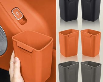 May include: A rectangular, open-top storage bin with a smooth finish and a small hook-like tab on the upper rim. The bin is shown in three colors: black, orange, and dark gray, with the orange version held against a matching orange car interior.