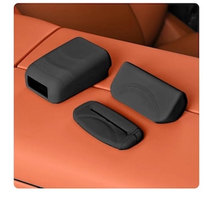 Puede incluir: Tres fundas protectoras de silicona negro mate para componentes interiores de automóviles. El conjunto incluye una carcasa rectangular con detalles acanalados, una cubierta de panel curva y una pieza rectangular plana con una ranura central.