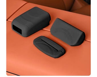 May include: Three matte black silicone protective covers for automotive interior components. The set includes a rectangular housing with ribbed detailing, a curved panel cover, and a flat rectangular piece with a central slot and arched lines.
