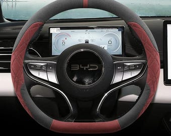 May include: A steering wheel cover featuring a combination of dark gray and deep red panels. The red sections display a diamond-stitched pattern, while a solid red stripe marks the top center. The cover is fitted over a black steering wheel with BYD branding.