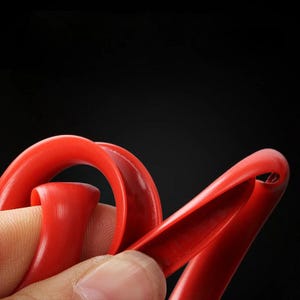 Puede incluir: Una tira de silicona flexible de color rojo brillante con una superficie lisa y curva. El material es maleable y muestra un canal hueco en forma de U a lo largo de su longitud, lo que demuestra su capacidad para doblarse y retorcerse.