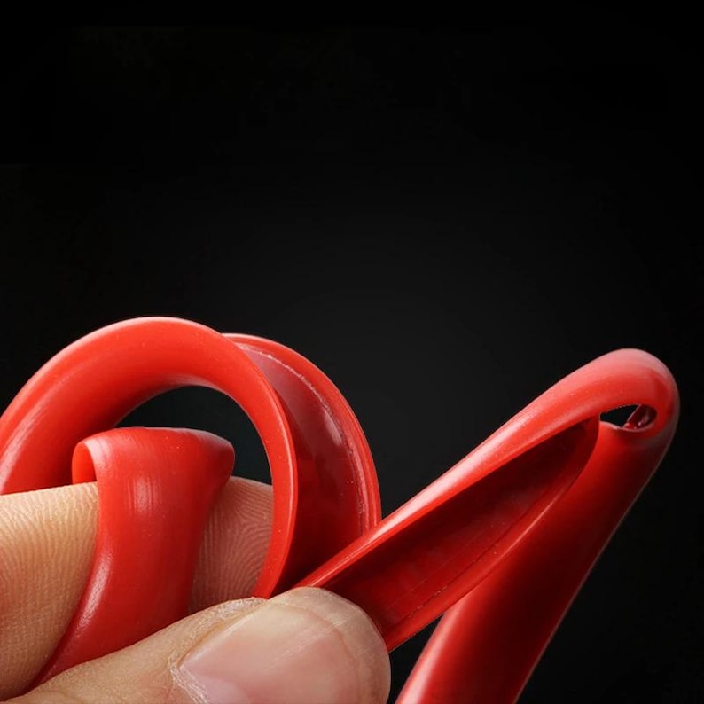 Puede incluir: Una tira de silicona flexible de color rojo brillante con una superficie lisa y curva. El material es maleable y muestra un canal hueco en forma de U a lo largo de su longitud, lo que demuestra su capacidad para doblarse y retorcerse.