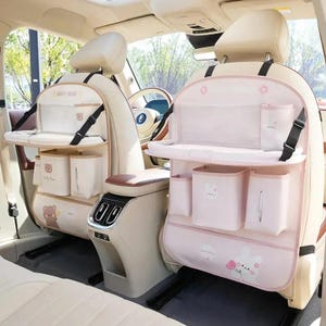 May include: Two car seat organisers attached to the back of front vehicle seats. Each organiser features a fold-down tray, multiple storage pockets, and a tissue dispenser. The left organiser has a bear graphic, while the right has a rabbit graphic.