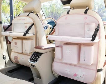 May include: Two car seat organizers attached to the back of front vehicle seats. Each organizer features a fold-down tray, multiple storage pockets, and a tissue dispenser. The left organizer has a bear graphic, while the right has a rabbit graphic.