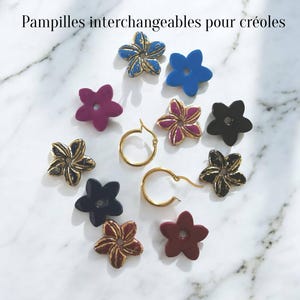 May include: A set of interchangeable flower-shaped charms in various colours including blue, purple, black, and gold-toned finishes, accompanied by two gold-toned hoop earrings. The text "Pampilles interchangeables pour créoles" is visible.