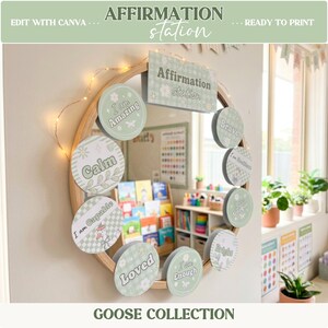 May include: A round mirror with a wooden frame is adorned with affirmation cards in a soft green color scheme. The cards feature phrases like "I am Amazing" and "Calm." The words "Affirmation Station" are displayed above the mirror. The words "Goose Collection" are at the bottom.