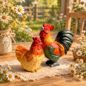 Pode incluir: Duas figuras de madeira esculpidas à mão de um galo e uma galinha. O galo apresenta uma crista vermelha brilhante, penas do pescoço laranja e amarelas e penas da cauda verde-escuras. A galinha é menor com plumagem laranja e amarela.