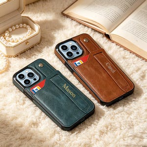 May include: Two smartphone cases with integrated card slots and snap-button straps. One case is dark green with the name Mason embossed, and the other is brown with the name Carol embossed. Both feature cutouts for triple camera lenses.