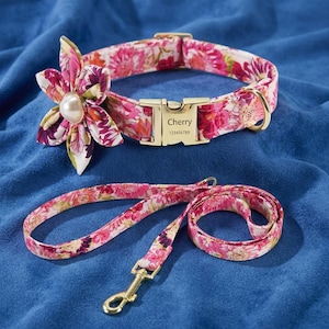 May include: A pink and white floral pet collar with a matching lead. The collar features a fabric flower with a central pearl accent and a gold-tone metal buckle engraved with the name Cherry and the number 123456789, plus a gold D-ring.