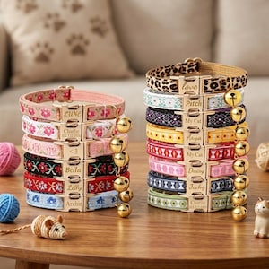 May include: Two stacks of fabric pet collars featuring various floral, geometric, and leopard print patterns. Each collar has a gold-toned metal buckle engraved with names like Lune, Charlie, Bella, Lilly, Archie, Love, Pitch, Aaya, and Daisy, plus a bell.
