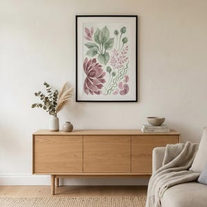 May include: A framed wall art print featuring a watercolour botanical illustration with various green leaves, pinkish-purple flower petals, and abstract wavy shapes on a white background, enclosed in a thin black rectangular frame.