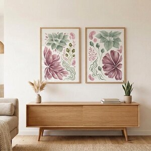 May include: Two framed wall art prints featuring botanical illustrations in muted tones of dusty rose, sage green, and cream. The artwork displays stylised floral and leaf motifs arranged in a vertical composition within light wood frames.