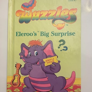 Könnte beinhalten: Ein Vintage-Kinderbuch mit dem Titel "Wuzzles: Eleroo's Big Surprise". Das Cover zeigt einen lila Elefanten-Charakter, der ein Los hält, eine Ukulele und den Text "Collector Series Book #3."
