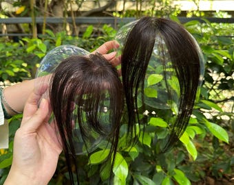 Peut inclure: Deux compléments capillaires brun foncé avec des mèches raides et une raie centrale, chacun fixé sur une base en plastique transparent et arrondi. Les postiches présentent de longues sections dégradées qui encadrent le visage.