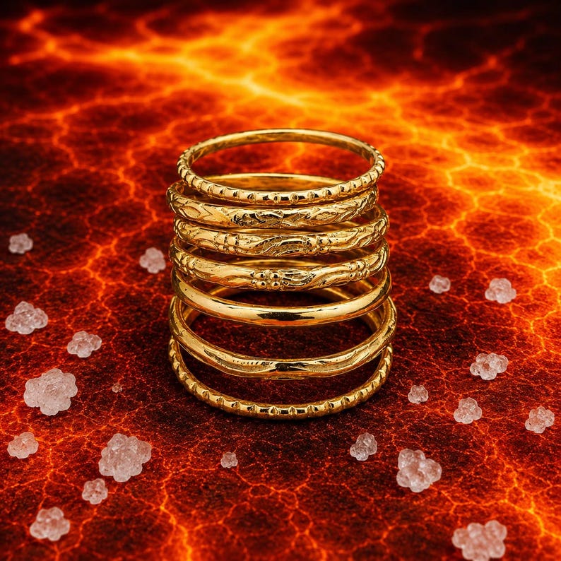 K&ouml;nnte beinhalten: Ein Stapel aus sieben goldfarbenen Ringen mit unterschiedlichen Texturen und Mustern, darunter glatte, perlenartige und gravierte Designs. Die Ringe sind vertikal in einer einzigen S&auml;ule angeordnet und zeigen eine polierte metallische Oberfl&auml;che.