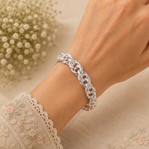 May include: A polished silver chain bracelet featuring a series of interconnected, rounded links. The bracelet has a high-shine metallic finish and a consistent, repeating pattern of circular loops that form a substantial, textured band around the wrist.