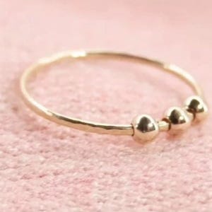 Könnte beinhalten: Ein dünner Goldring mit drei kleinen, glatten, runden Goldperlen, die entlang der Ringschiene angeordnet sind. Das Metall hat eine polierte Oberfläche und der kreisförmige Ring ist so gestaltet, dass er am Finger getragen werden kann.