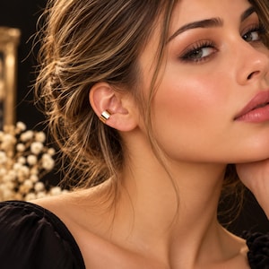 May include: A smooth, polished gold-tone ear cuff worn on the cartilage of the ear. The jewelry piece features a simple, wide band design with a reflective metallic finish that sits securely along the outer edge of the ear without requiring a piercing.