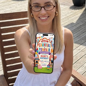 May include: A smartphone displaying a colorful digital carnival and funfair birthday invitation. The screen features text reading Step Right Up! You're Invited To A Carnival & Funfair Extravaganza To Celebrate Name's Birthday, with graphics of tents, balloons, and a Ferris wheel.