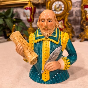 Könnte beinhalten: Eine Keramikbüste von William Shakespeare in einem blaugrünen Wams mit gelbem Besatz. Die Figur hält eine Schriftrolle mit der Aufschrift 'Alas poor Yorick I knew him Horatio' in der einen und eine silberne Feder in der anderen Hand.