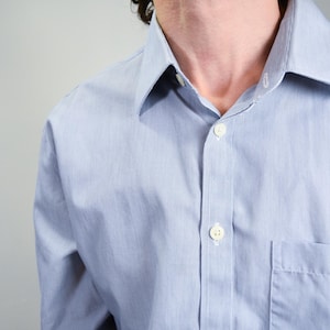 May include: A light blue dress shirt with a white button-down collar and a single pocket on the left side.