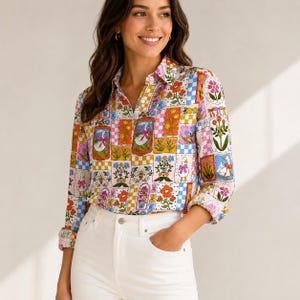 Puede incluir: Una camisa de manga larga con botones que presenta un colorido patrón de patchwork de gansos blancos con lazos rosas, diversos arreglos florales, abejas y cuadrados a cuadros en tonos naranja, rosa, azul y verde sobre un fondo blanco.