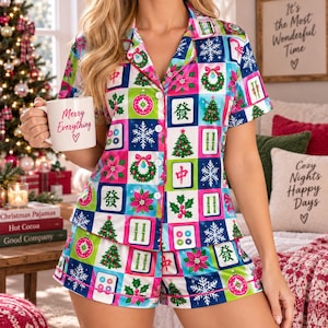 May include: A short-sleeve button-down pajama shirt and matching shorts set featuring a colorful grid pattern of Christmas trees, snowflakes, poinsettias, wreaths, and mahjong tiles. The shirt has a white mug with the text Merry Everything.