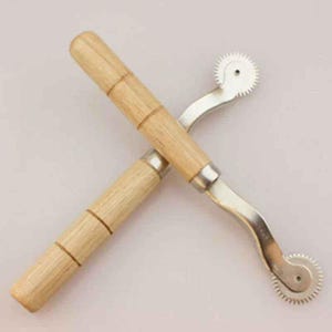 May include: Two sewing tracing wheels with light-colored wooden handles and silver-toned metal shafts. Each tool features a small, circular, serrated metal wheel at the end, designed for marking fabric patterns with precision and consistent spacing.