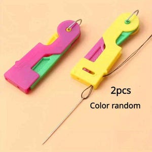 May include: Two plastic needle threaders with a retractable design. One tool is primarily magenta with green accents, and the other is yellow with green accents. Each features a thin metal wire loop for threading. Text reads 2pcs Color random.