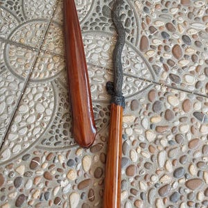 Puede incluir: Un keris de madera con una hoja ondulada de color oscuro y un mango de madera marrón claro liso y pulido. El keris viene acompañado de una funda de madera pulida a juego, separada, de forma cónica y alargada.